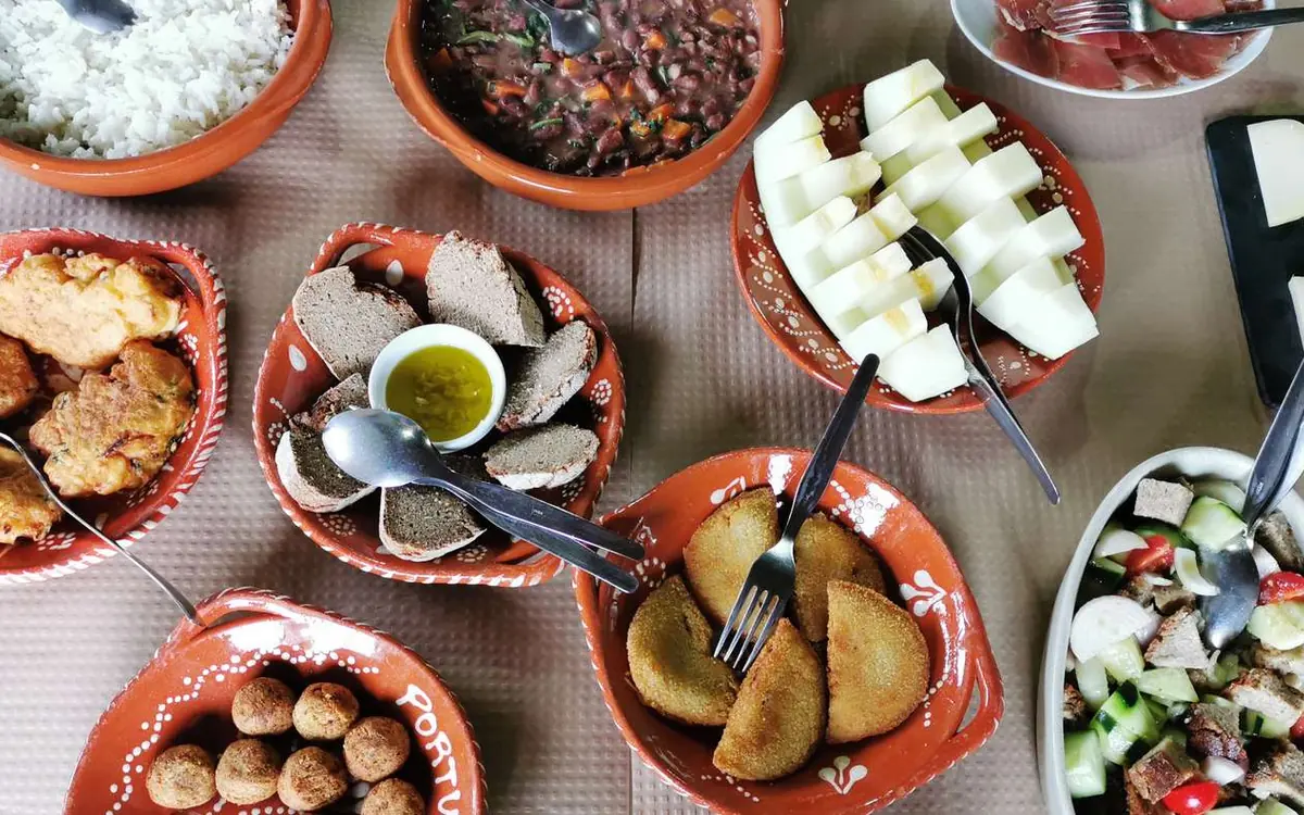 Terracotta bowls of rice, beans, bread and fritters crowded on a table, from above