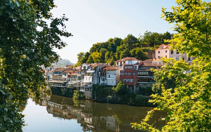 Old houses in a river town reflected in still green water, trees on both banks
