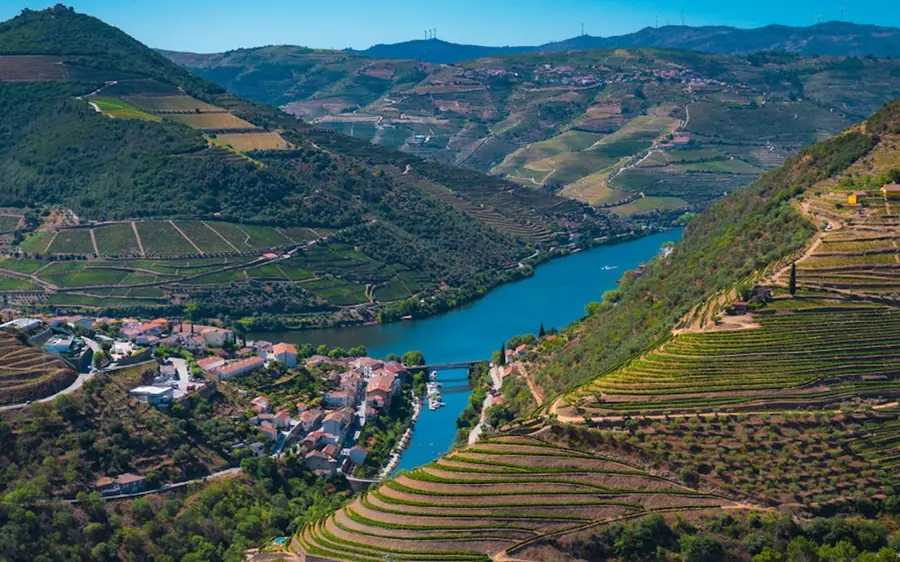 A wide river bend below terraced vineyards, a small village on the near bank