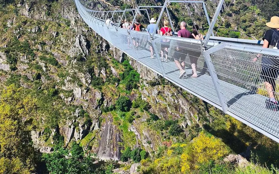 Walkers crossing a narrow suspension footbridge high above a rocky gorge
