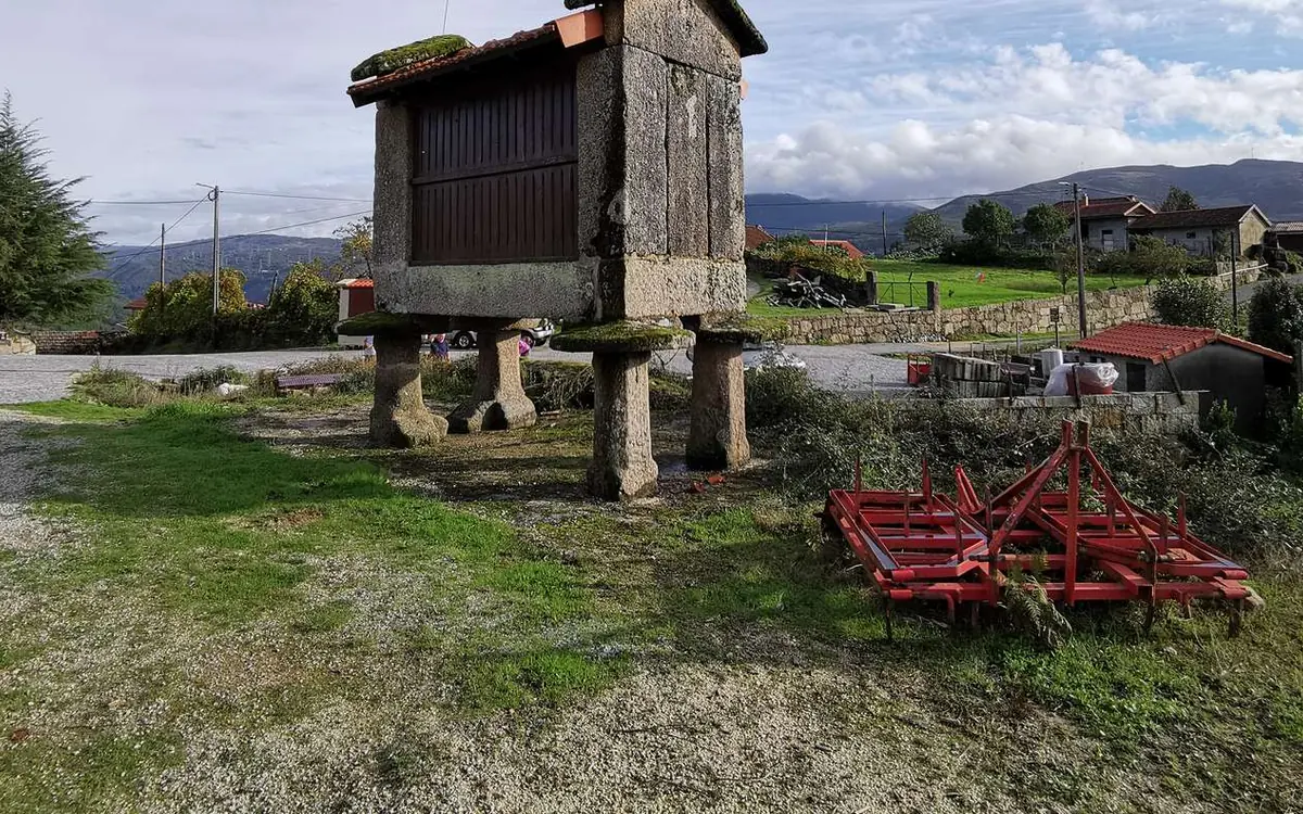 A stone granary raised on legs with a village and green hills behind it
